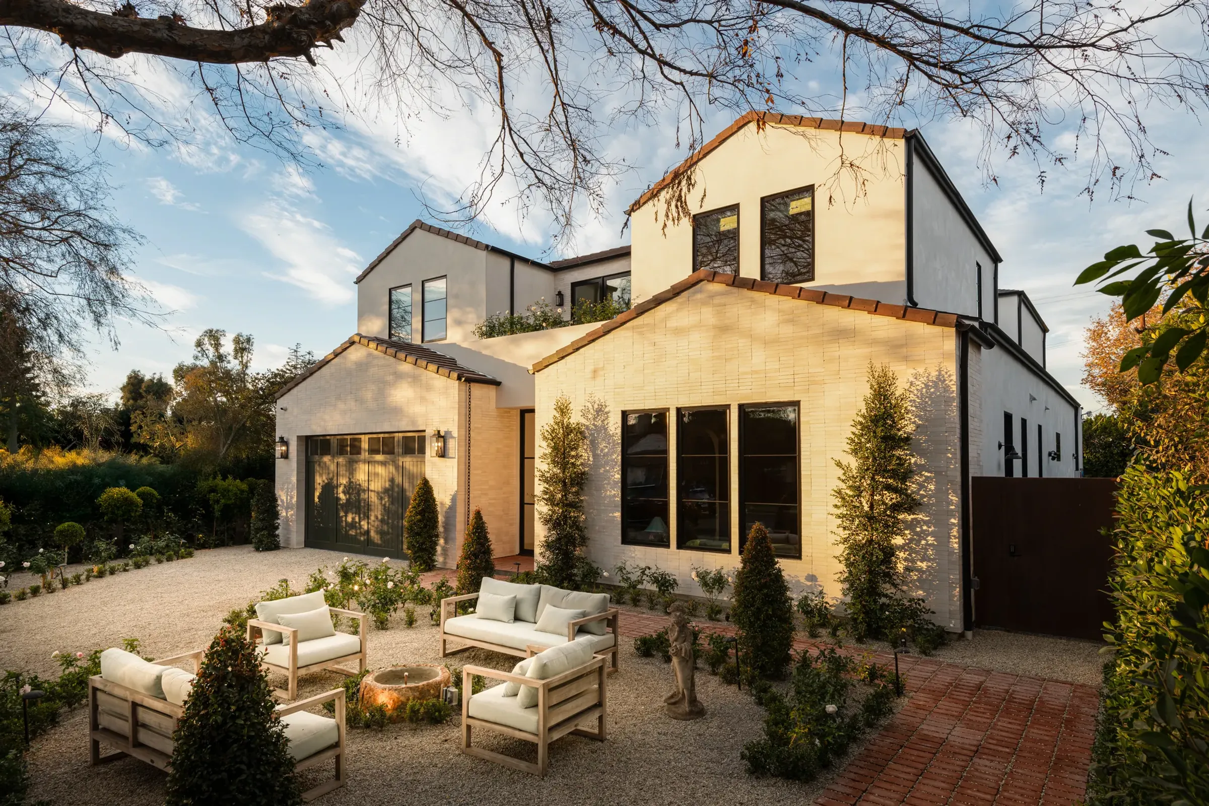 New white brick farmhouse with a gravel courtyard and lounge chairs in afternoon sun