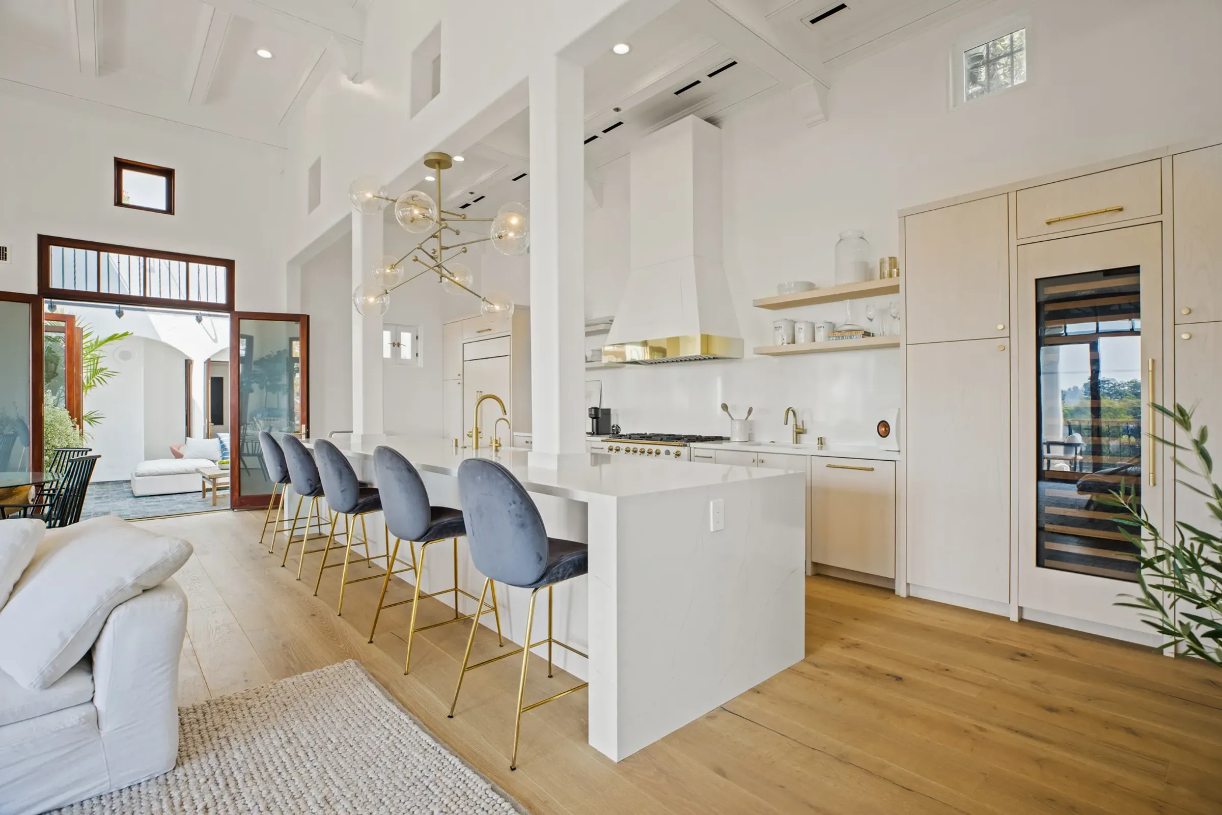 White kitchen with brass fixtures, a long island and blue velvet stools